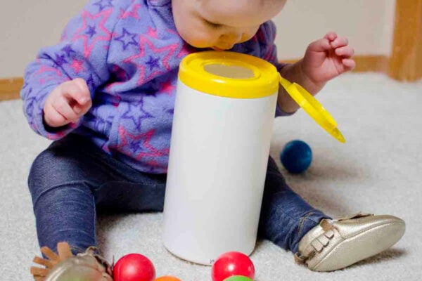A baby looks into a wipes container for the ball she dropped