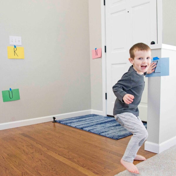 A child turns to the camera as they tap a construction paper Z taped to their foyer in an Alphabet Activity from Busy Toddler.