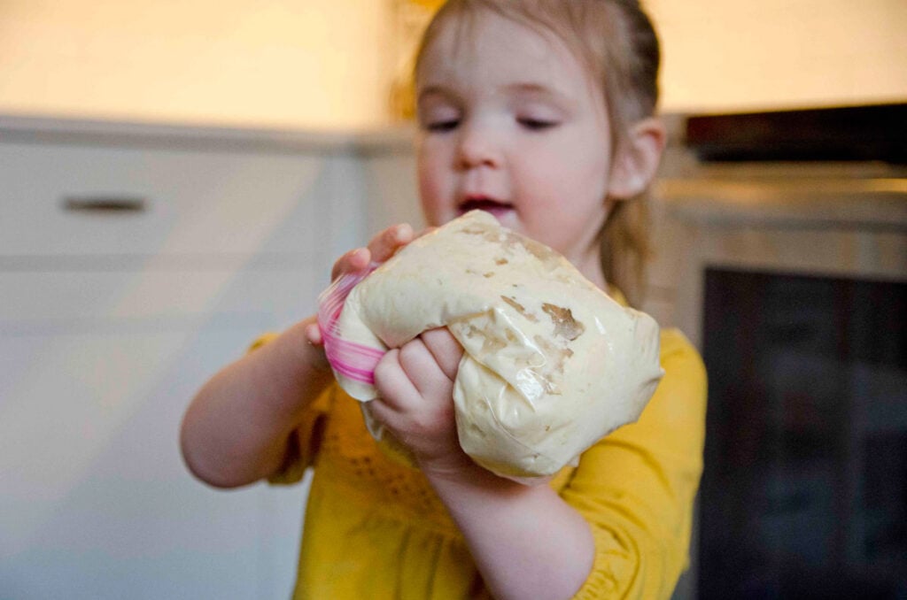 A child holds a bag a bread dough while making bread in a bag