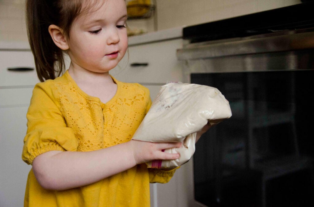 A 3 year old inspects a bag of bread dough.