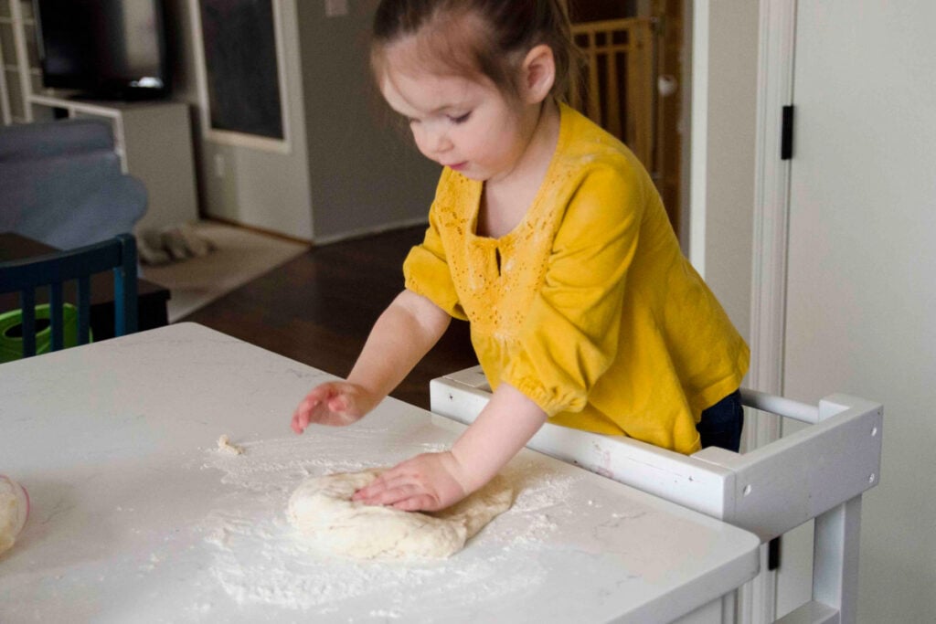 A preschooler kneads dough while making bread.