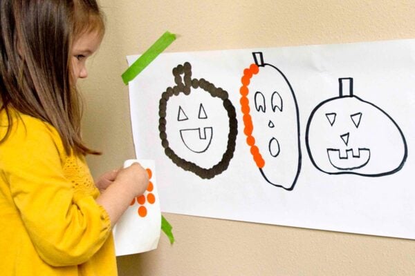 A child peels an orange dot sticker to place on a pumpkin outline