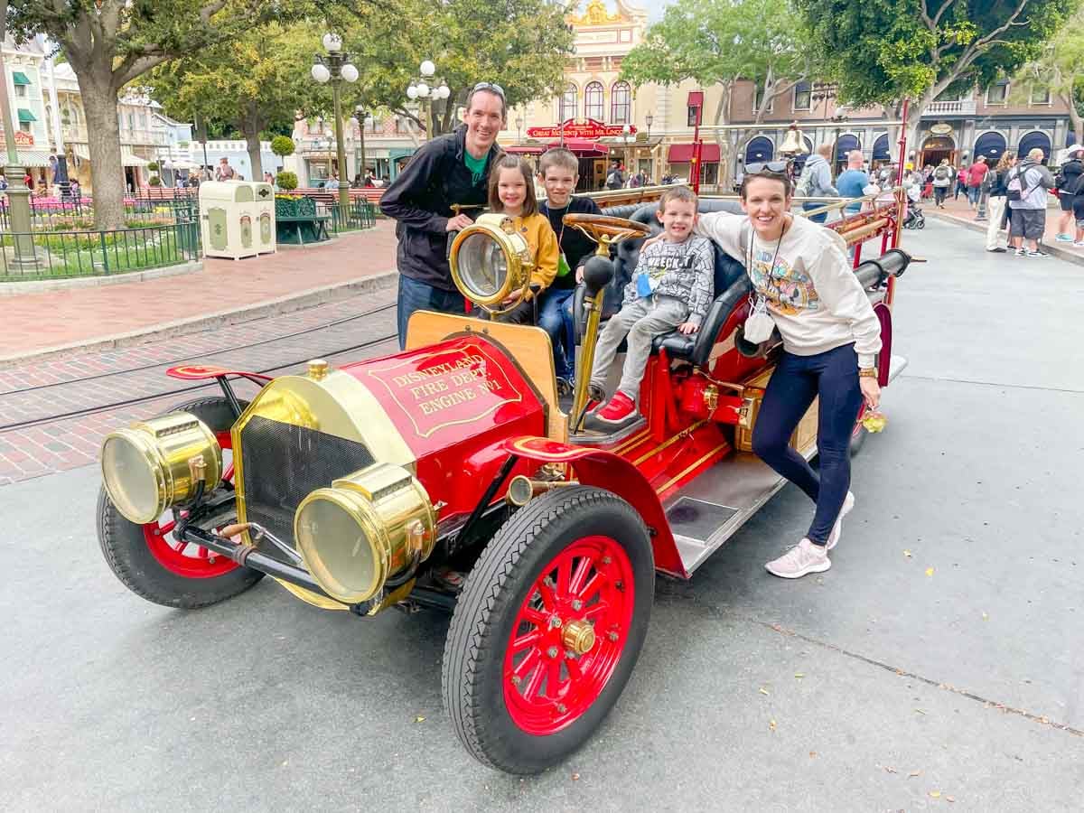 A family sits on the Disneyland red fire truck while visiting the park.