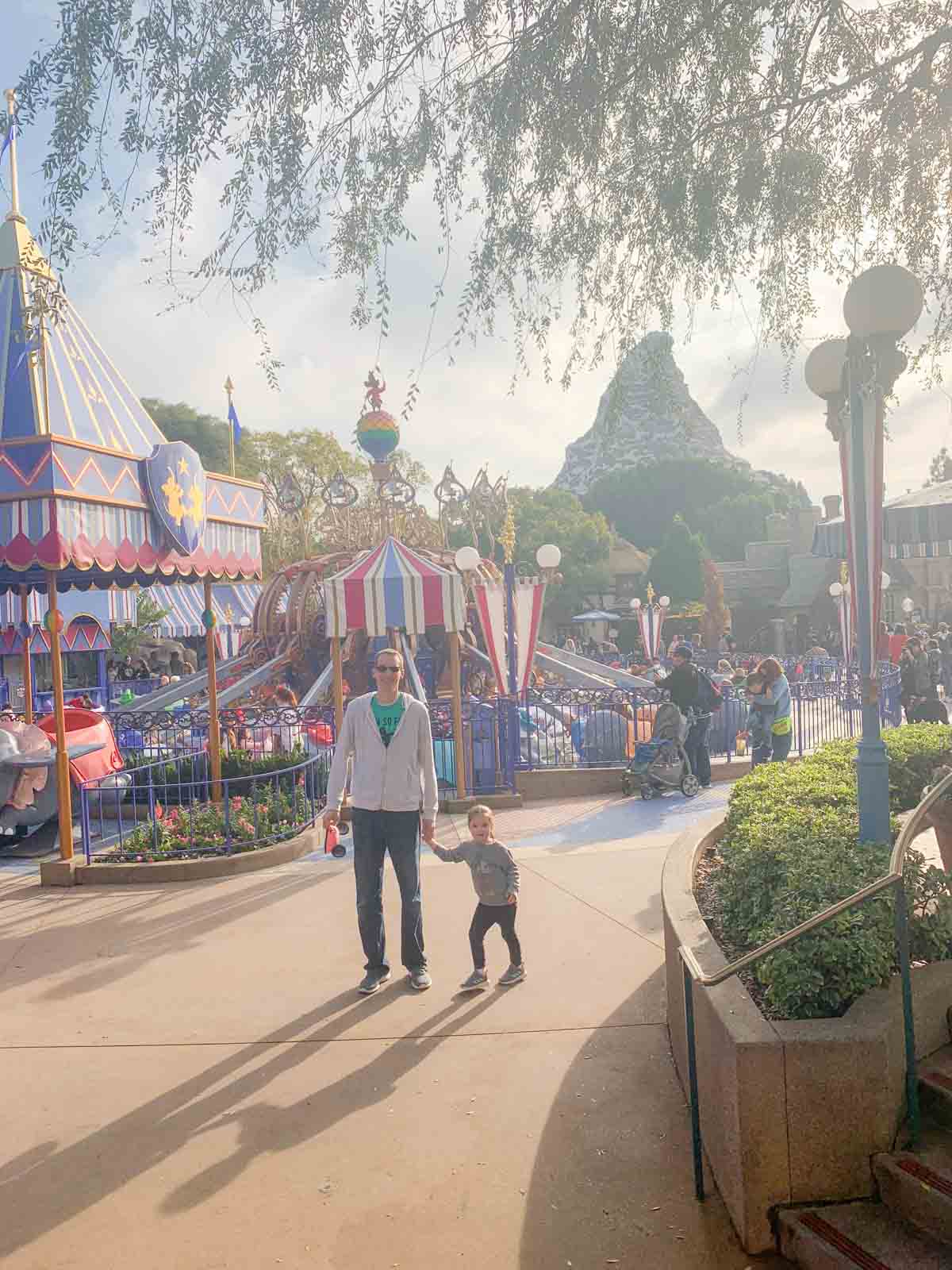A backlit photo of a father and daughter in Disneyland's Fantasyland. The Matterhorn is behind them.