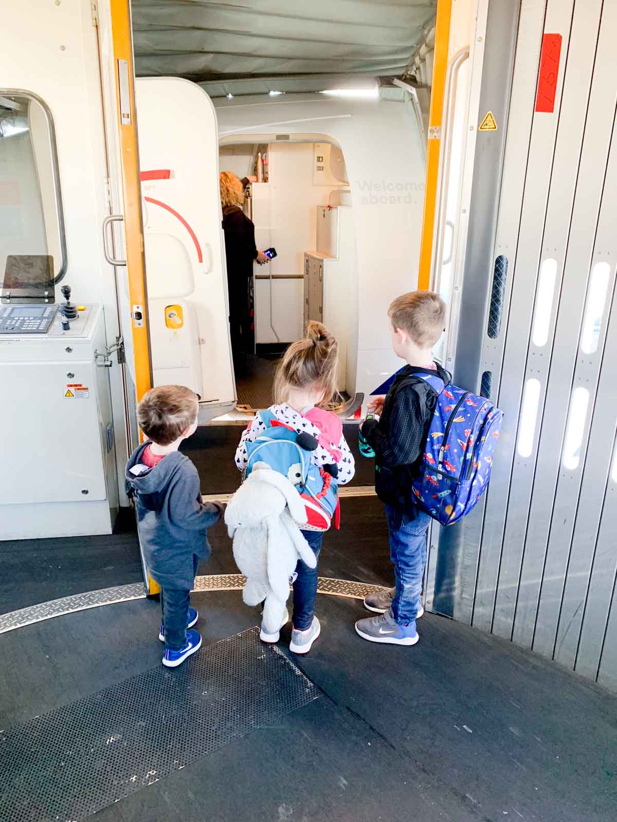 Three kids stand at a jet way waiting to board an airplane to Disneyland.