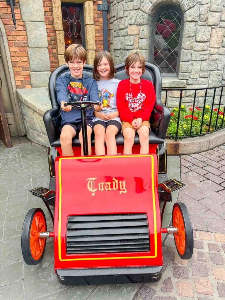 Three kids sit in the Mr Toad's wild ride cart at disneyland.