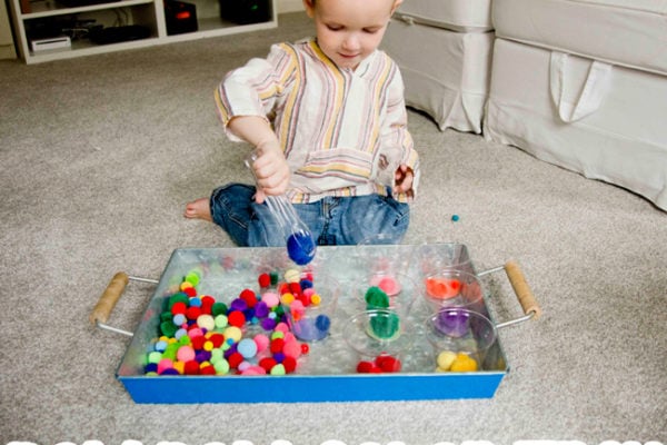 A toddler doing a pom pom color sorting activity using tongs and pom pom balls by Busy Toddler