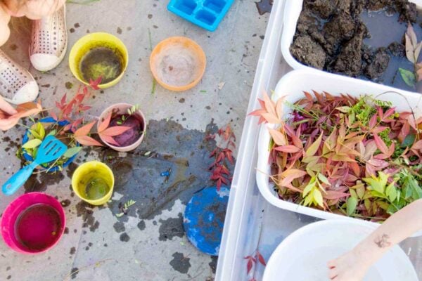 Overhead view of a DIY mud kitchen with dirt, water, and leaves. Two children are present but just off frame.