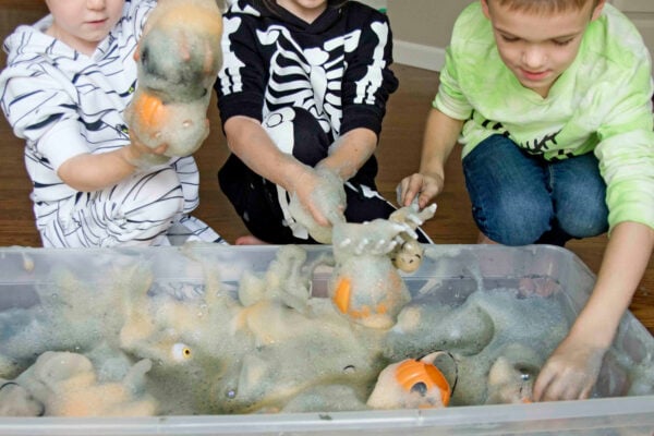 3 kids playing with orange and black bubble foam in a sensory bin