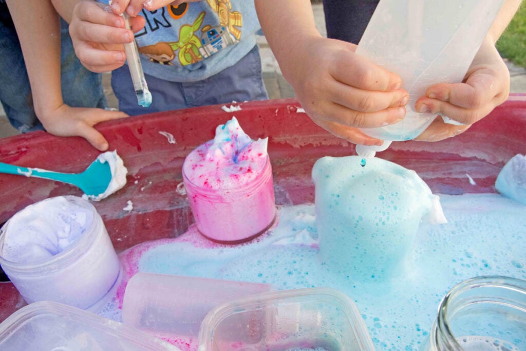 A child squeezes vinegar into a jar of "potions" aka baking soda and soap.