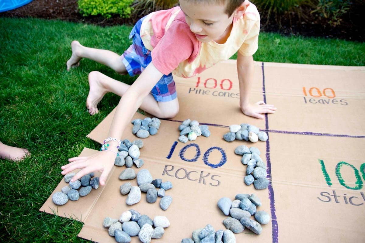 A boy leans over to count groups of rocks in piles of 10 to make 100.