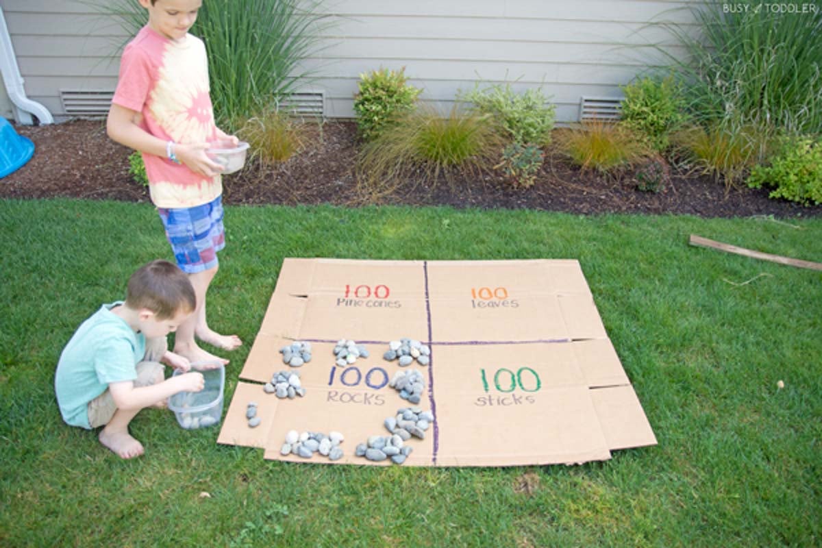 Two boys sit next to flat cardboard split into groups of 100, sorting rocks in piles of 10.