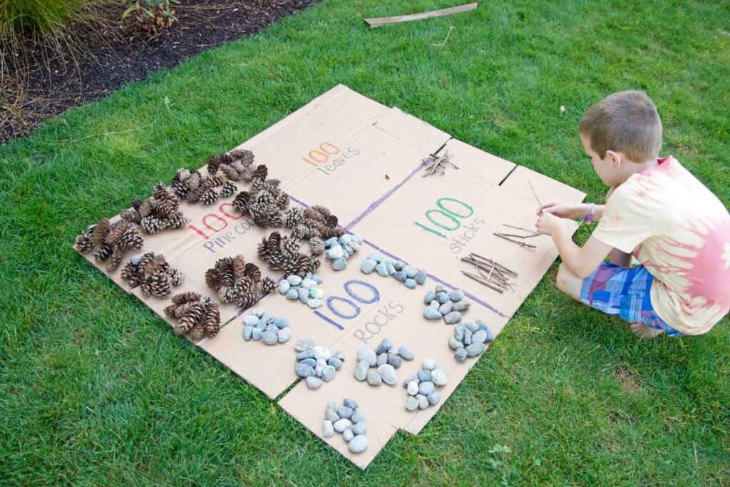 A child sits counting sticks in groups of 100. They are laying them on flat cardboard.