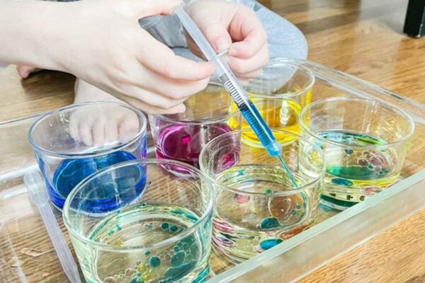 Child adding colored water to cups of vegetable oil