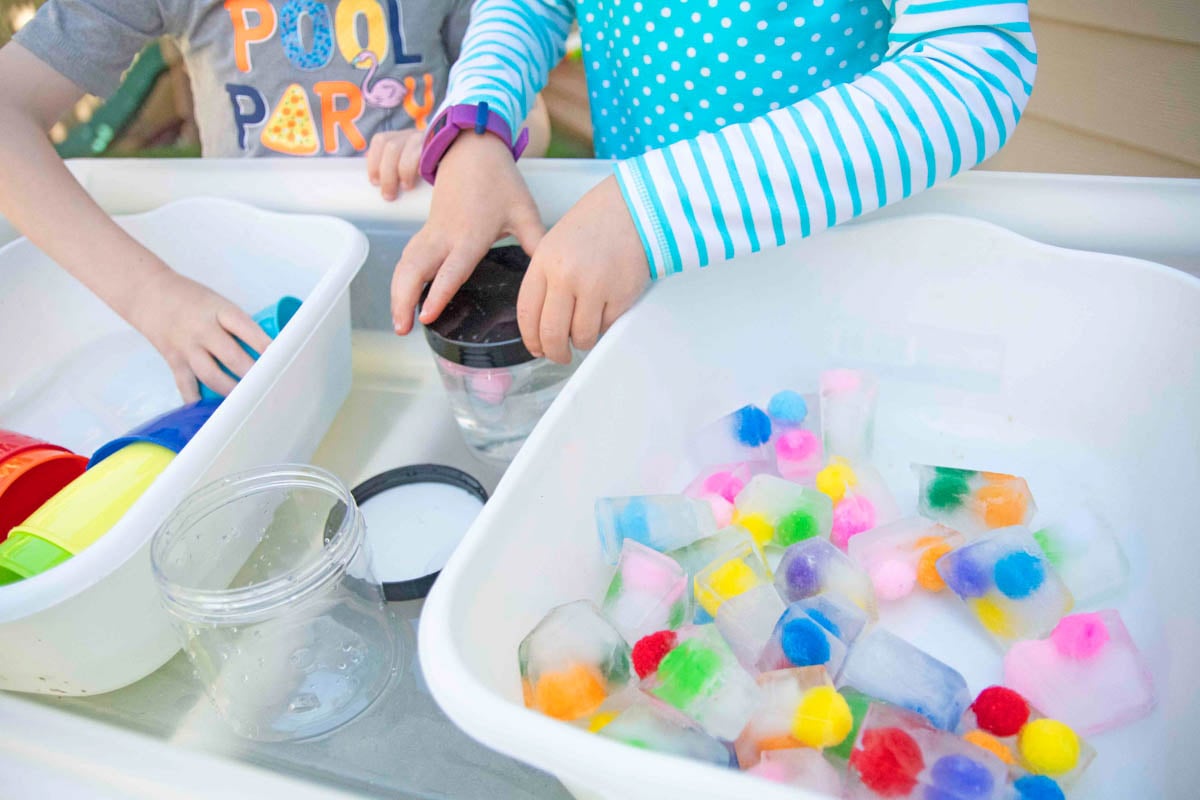 A child screws on a black lid next to frozen pom pom ball ice cubes.
