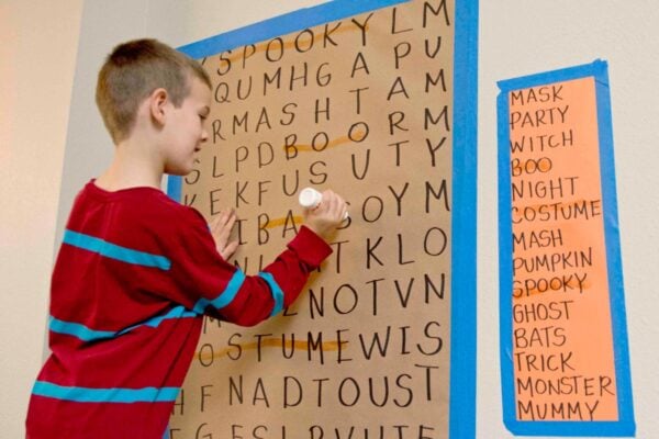 A child stands at a giant word search. Blue tape holds up the word search.