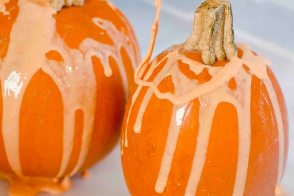 Pumpkins in a sensory bin being covered in orange oobleck by a toddler