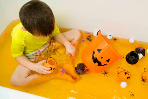 Child sitting in an orage water tub with Halloween toys around him.