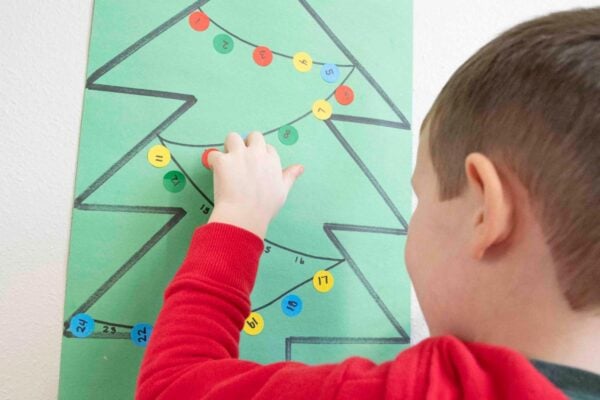 A child reaches to add a dot sticker to a number line on a green construction paper tree.