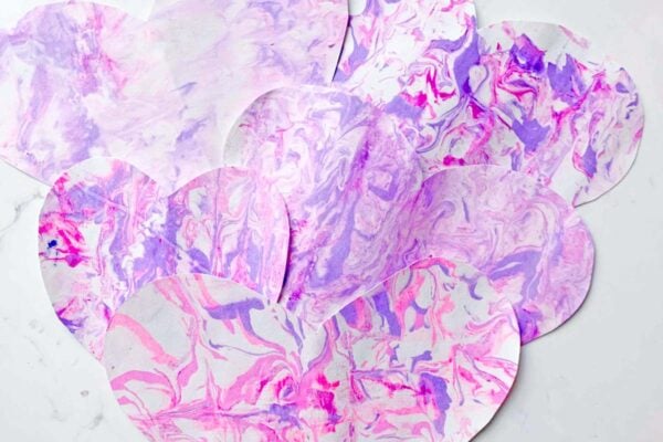 A set of shaving cream marble hearts sits on a white countertop. The marble pattern is made of purples and pinks.