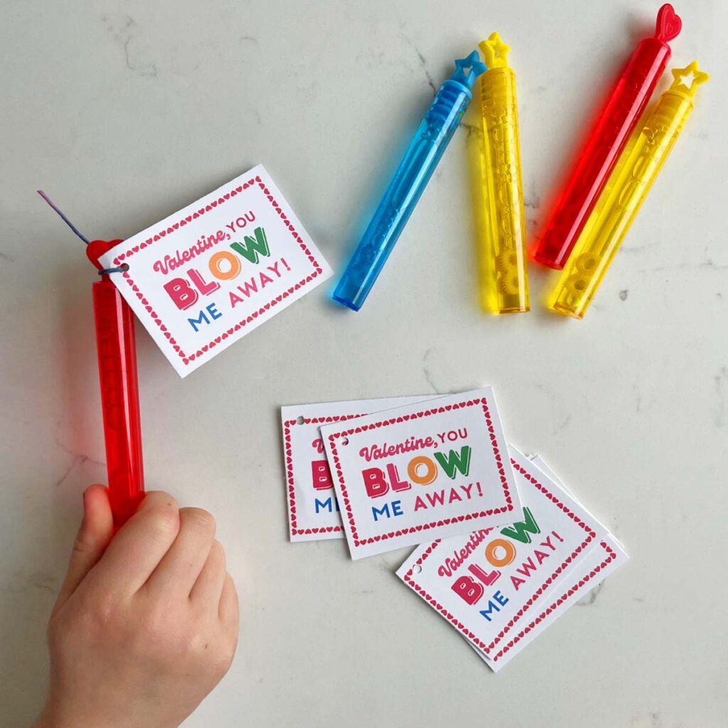 Free Valentine printables with bubbles. The printable says "Valentine, you blow me away." A child's hand is holding the bubbles.