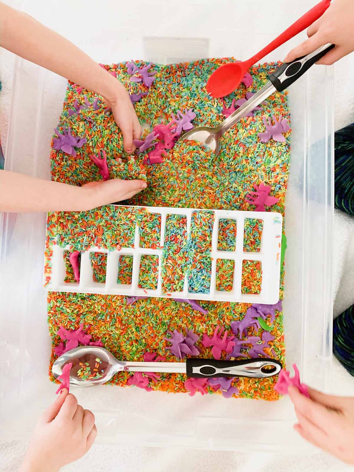 A group of kids playing in a bin of rainbow rice.