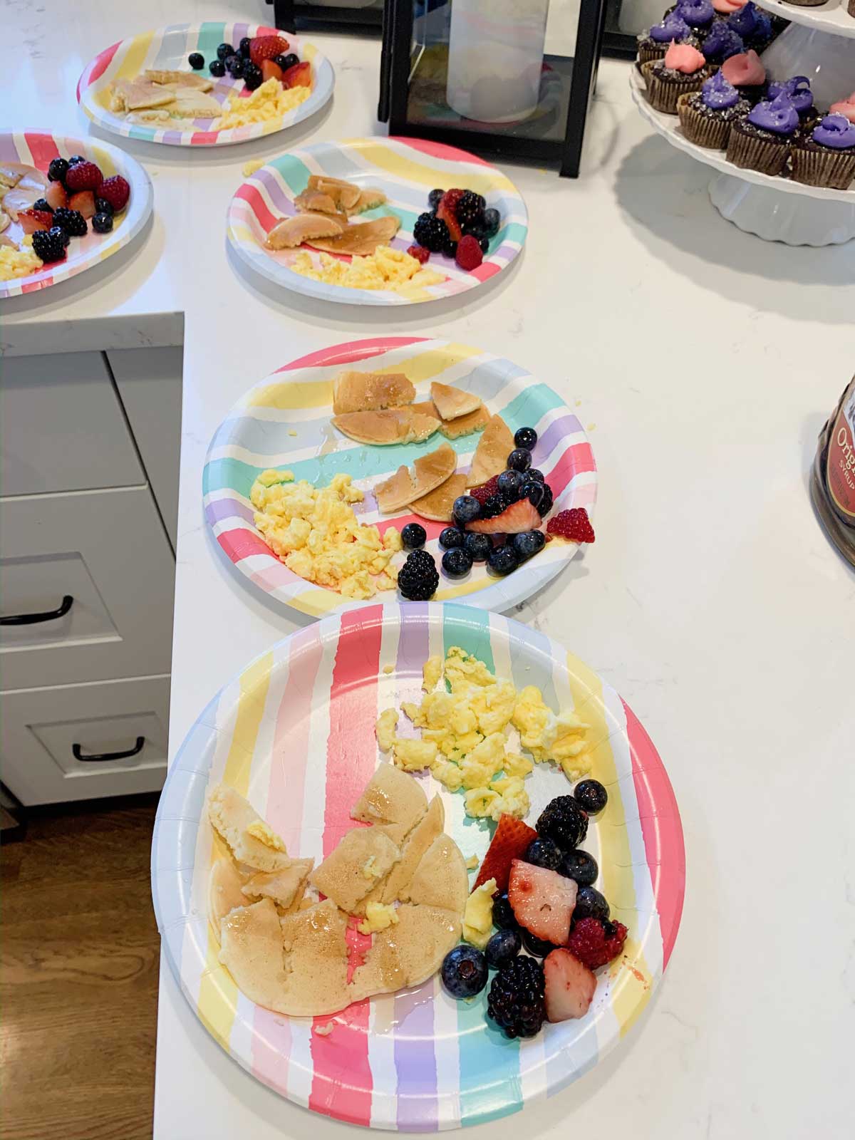 Paper plate full of pancakes, scrambled eggs, and a fruit salad.