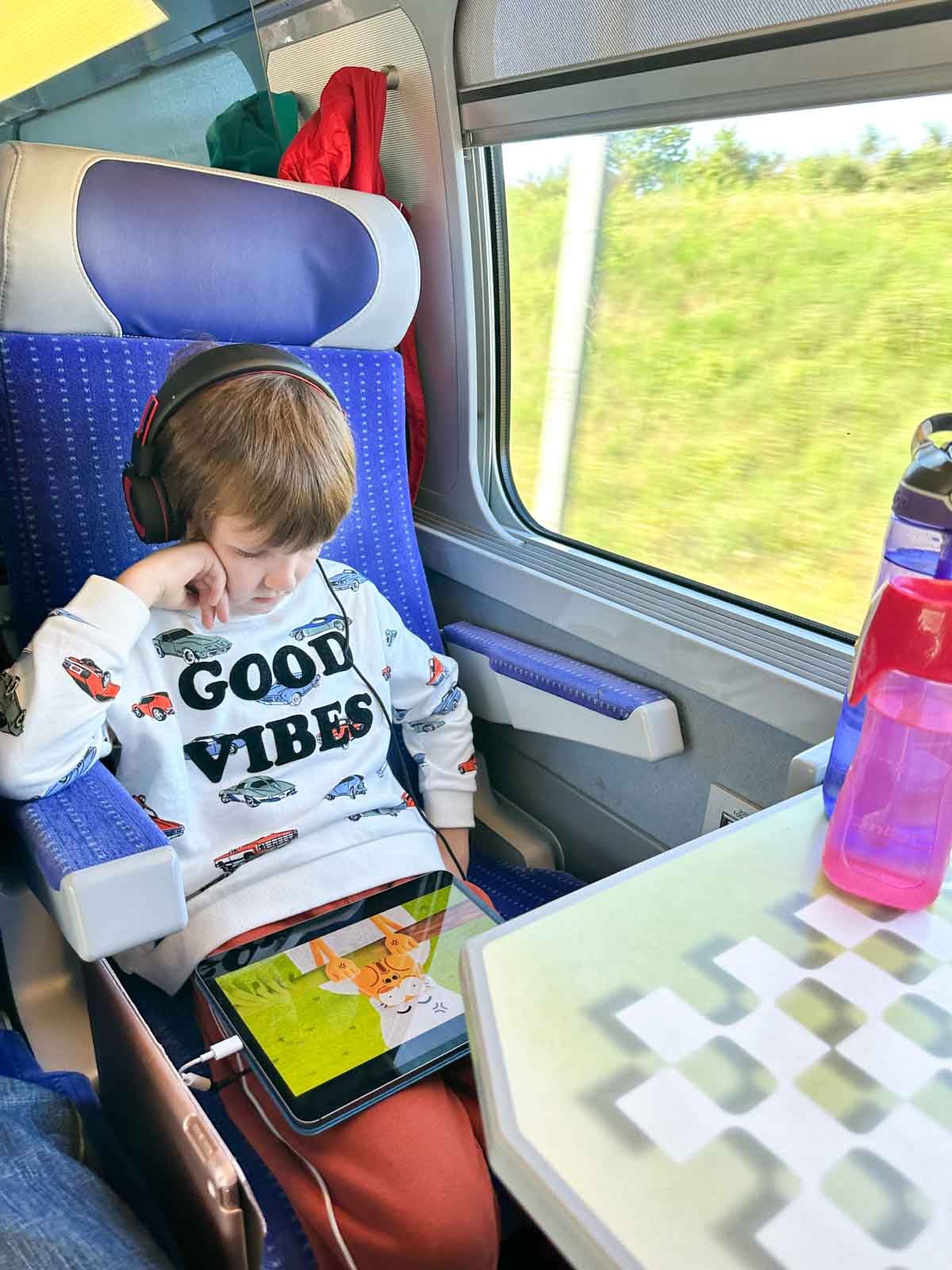 A child sits on a train wearing a "good vibes" sweatshirt. He is traveling from France to Switzerland.