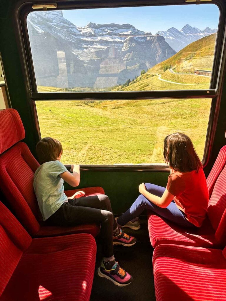 Two children look out the window of a train on a Swiss Alps vacation.