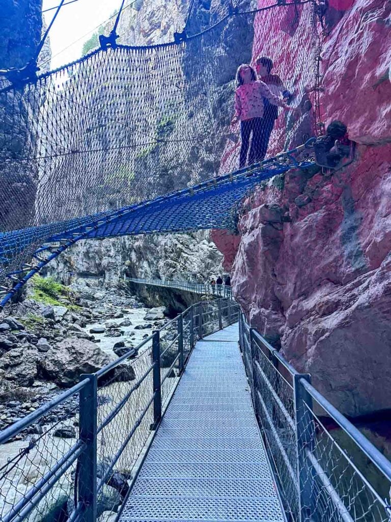 Two kids on a spiderweb net over a river in a canyon.