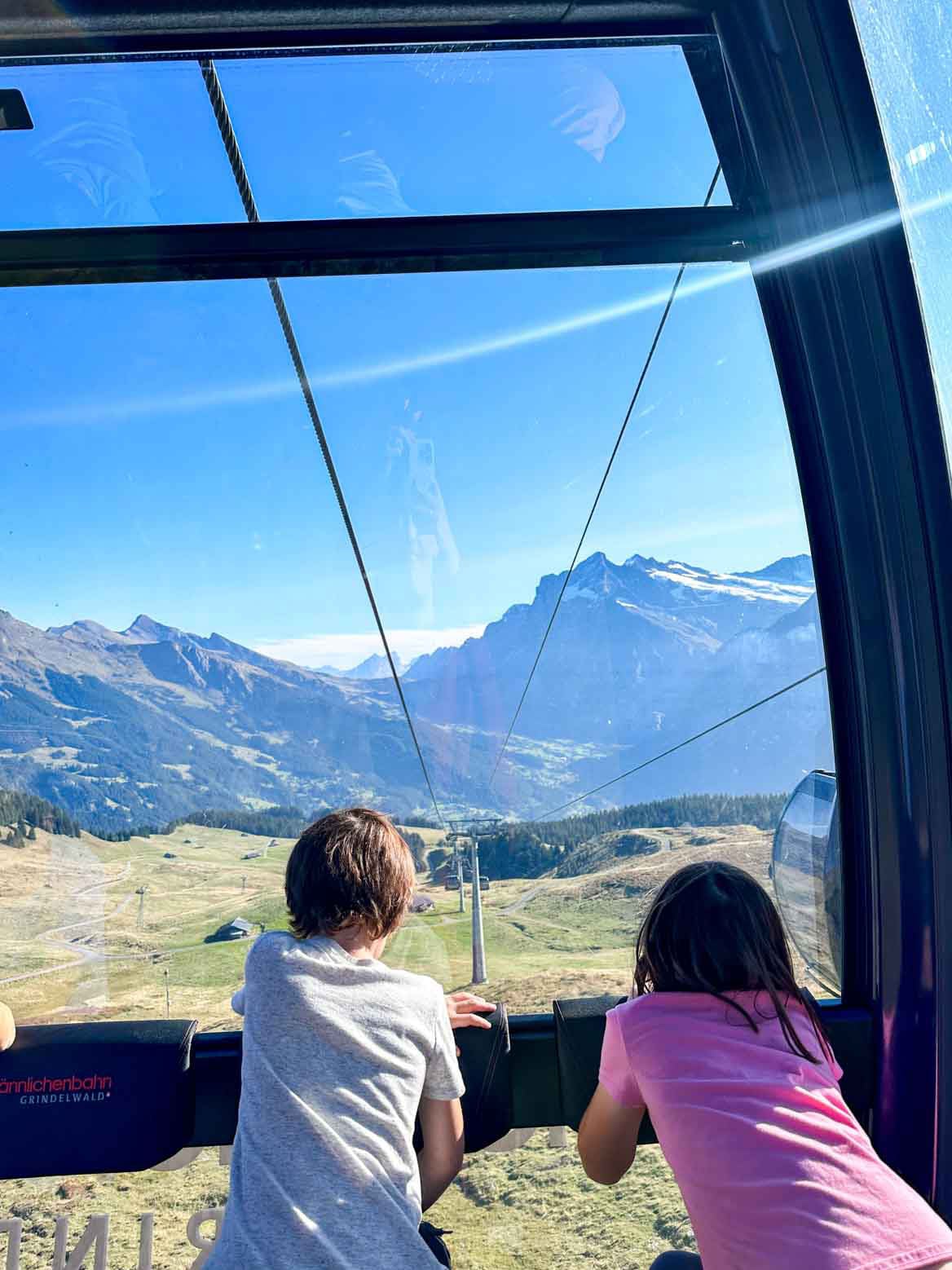 Two children look out the window of a gondola.