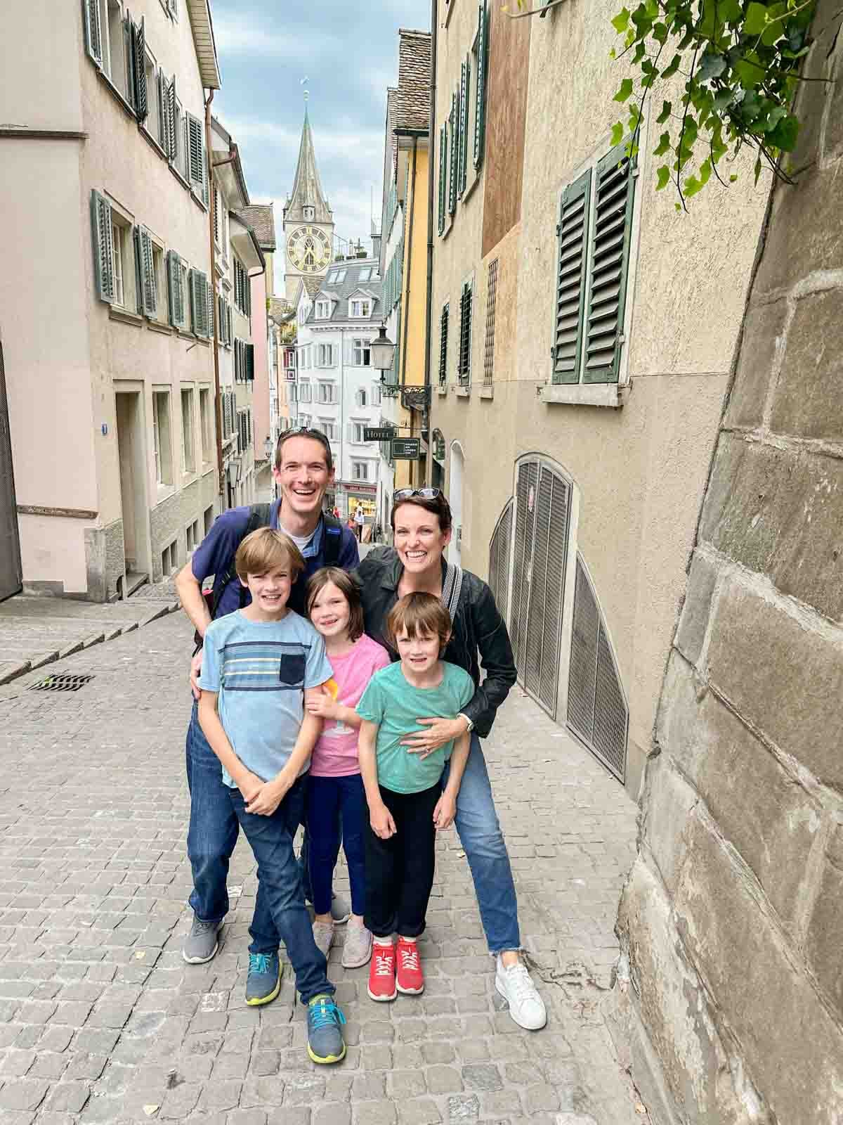 A family stands on a cobblestone path with a famous clock and buildings in Zurich behind them.