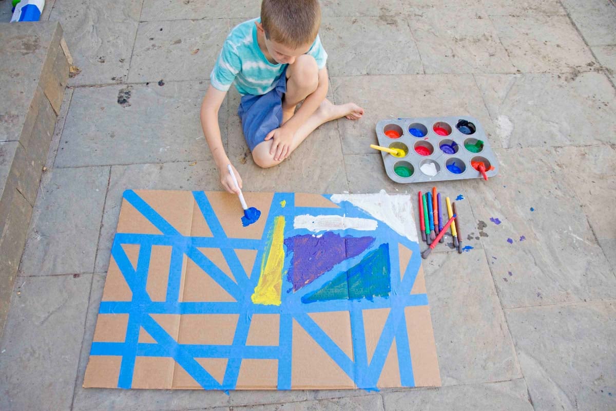 A child adds red paint to a tape resist project in his backyard.