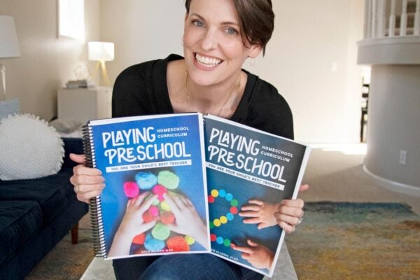 Author Susie Allison holds copies of her Playing Preschool homeschool preschool program. She is sitting in a living room.
