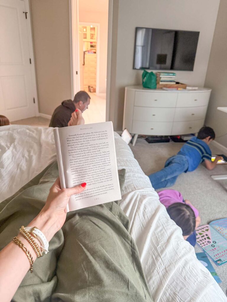 A mom holds a book to read aloud while her children and husband sit to listen