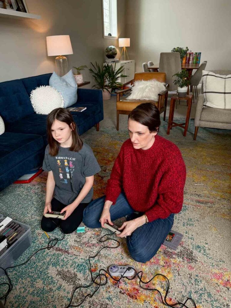 A mom and daughter play Nintendo together on the floor of a living room.