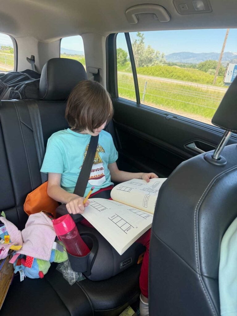 A child quietly reads a puzzle book in the car. There is a water bottle next to them.
