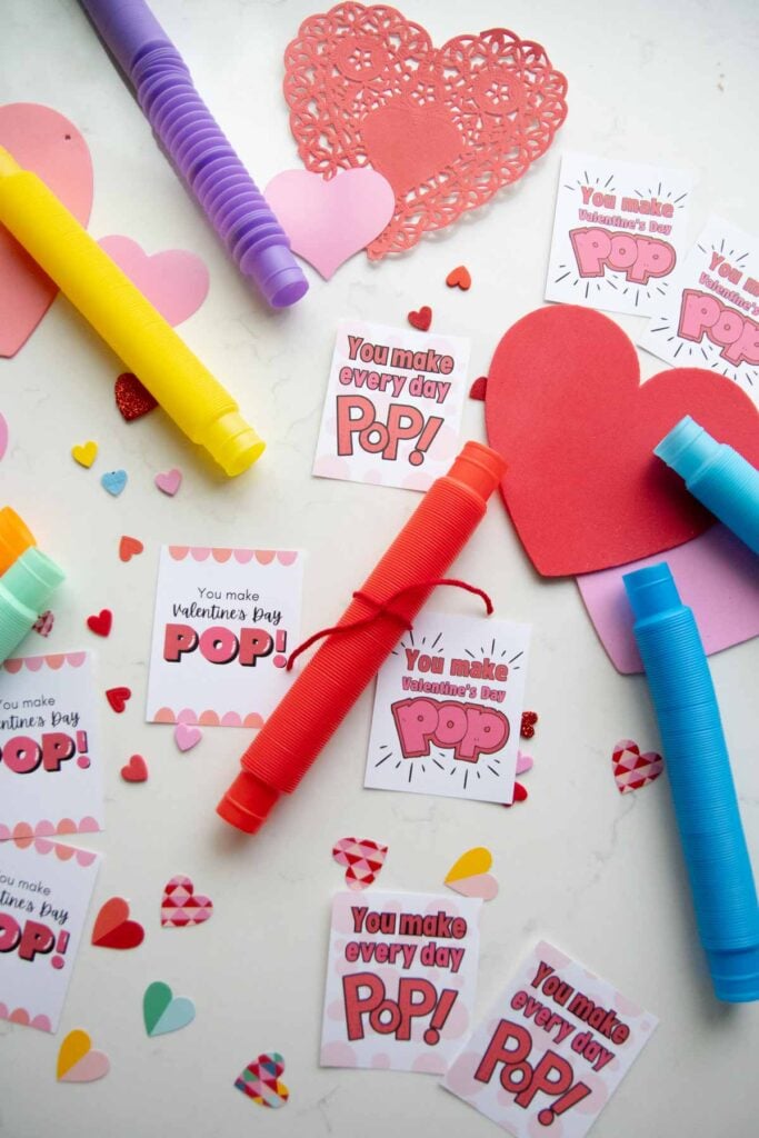 A flat lay for Valentine's day cards. There are three styles of Valentine's day card set amongst pop tubes and heart decorations.
