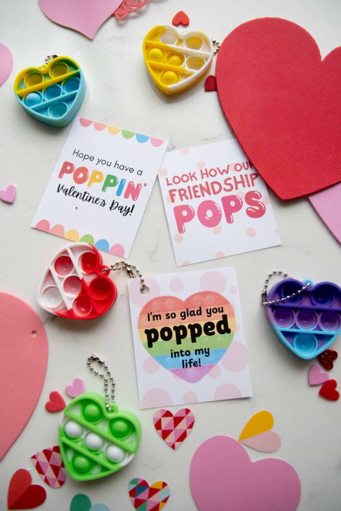 Valentine flat lay on white with three different Valentine cards for kids to use with pop fidget key chains.