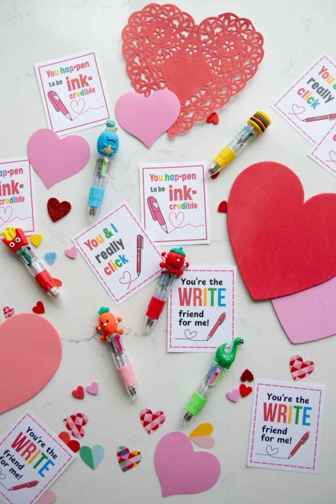 A flat lay on a white counter of Valentines with "write" puns. The treat is a fun multi ink mini pen.