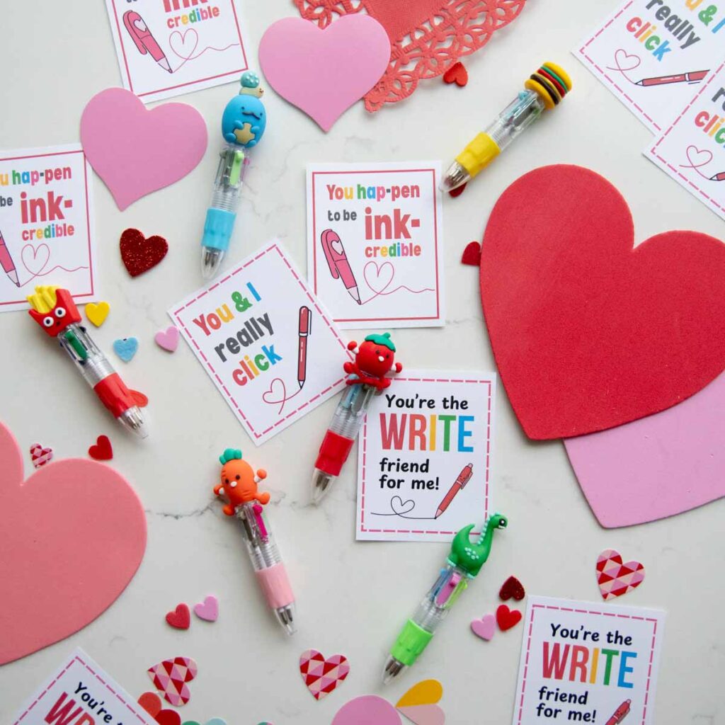 A flat lay on a white counter of Valentines with "write" puns. The treat is a fun multi ink mini pen.