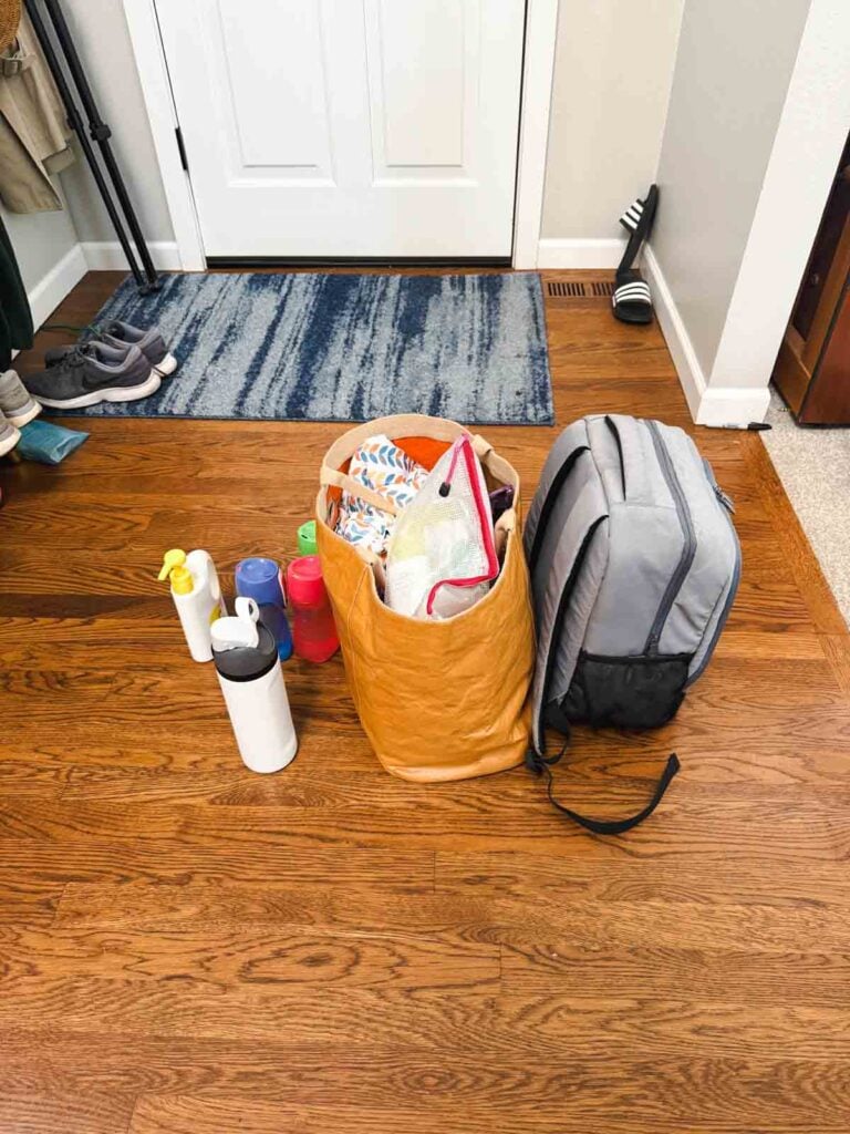 A collection of bags and water bottles at the front door of a home.